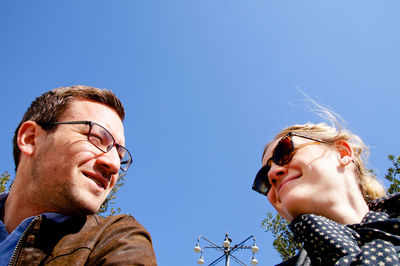 Low angle view of smiling couple against clear blue sky