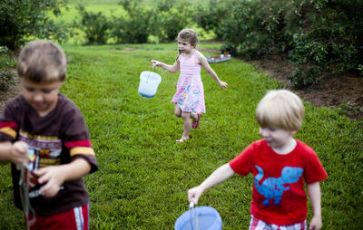 Siblings carrying buckets while walking in blueberry farm