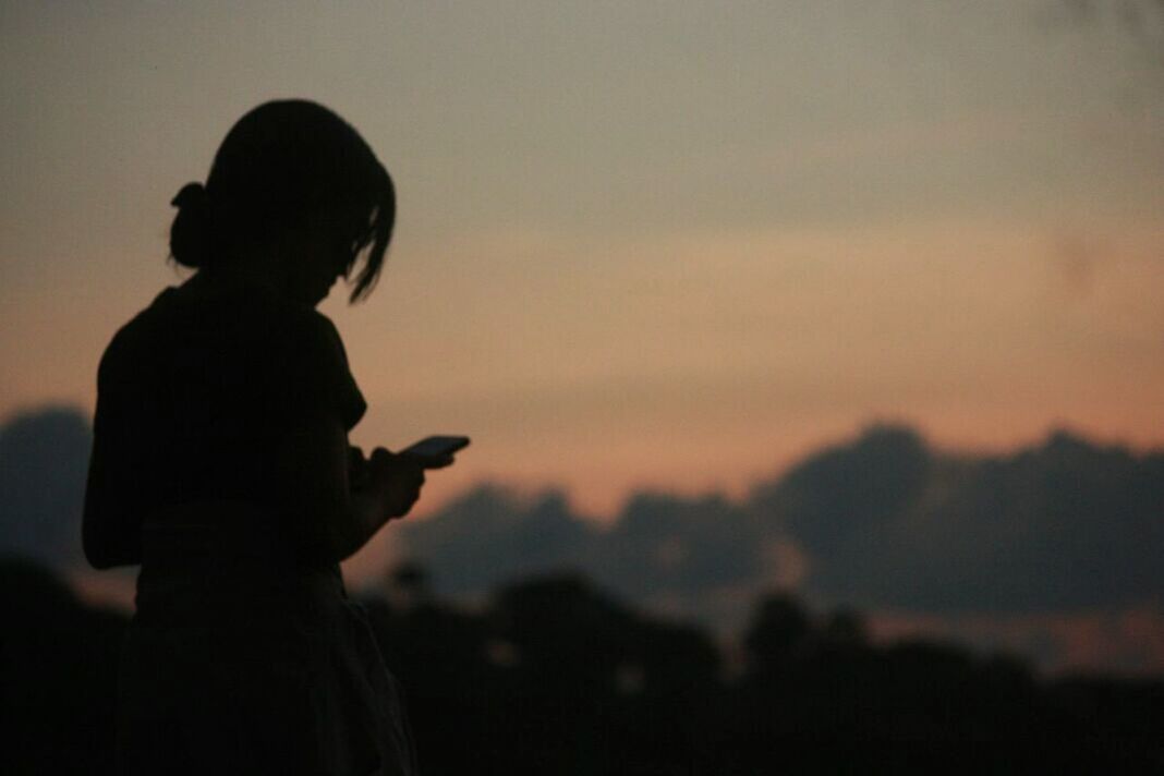 sunset, silhouette, sky, real people, leisure activity, lifestyles, standing, side view, one person, technology, focus on foreground, adult, nature, photography themes, three quarter length, wireless technology, waist up, smart phone, men, outdoors