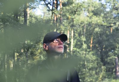 Man looking away while standing against trees in forest