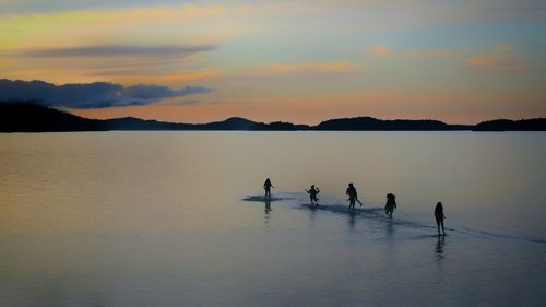 Silhouette people on shore against sky during sunset