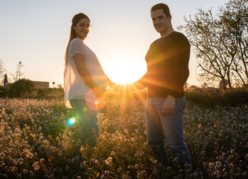 Friends standing on field against sky during sunset