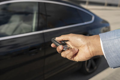 Businessman unlocking car with key on sunny day