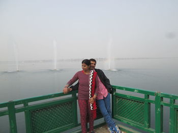 Full length of friends standing on railing against sea