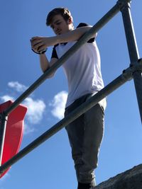 Low angle view of man leaning on railing against blue sky