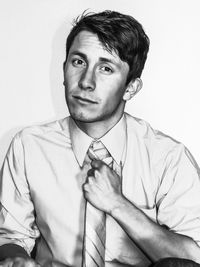 Close-up portrait of young businessman holding necktie against white background