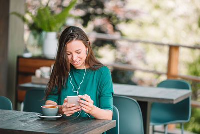 Young woman using phone while sitting on table