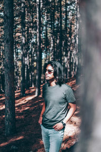 Young man standing by tree in forest