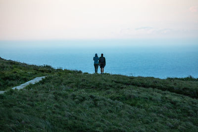 Rear view of people standing on cliff against sea