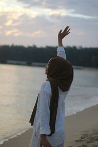 Rear view of woman standing at beach during sunset