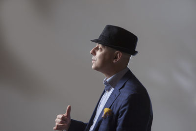 Side view of mature businessman showing thumbs up against gray background