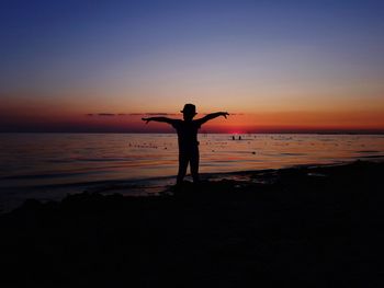 Silhouette man standing on beach against sky during sunset