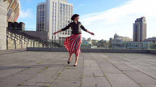 Happy woman wearing striped skirt and jacket on footpath in city