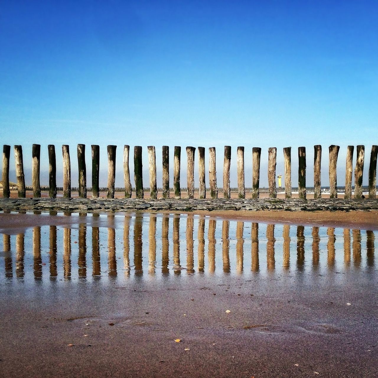 water, sea, clear sky, beach, in a row, wooden post, blue, copy space, tranquility, tranquil scene, horizon over water, pier, nature, sand, scenics, wood - material, beauty in nature, fence, shore, reflection