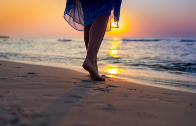 Low section of woman on beach during sunset