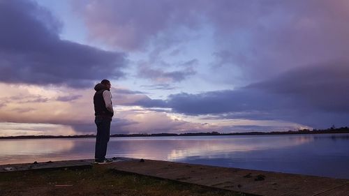 Woman standing by sea against sky during sunset