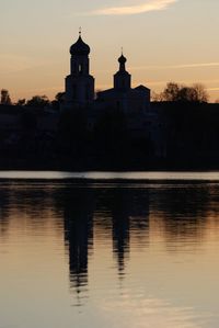 Silhouette of building by lake during sunset