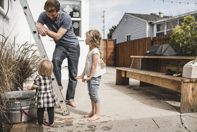 Father looking at daughters playing with water outside house