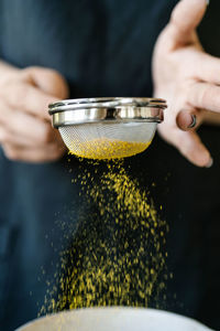 A girl in a linen apron sifts spices into a bowl on a marble table. there are other spices nearby.