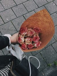 Cropped image of person holding rose bouquet on paved footpath