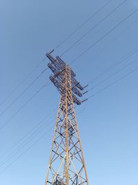 Low angle view of electricity pylon against clear blue sky