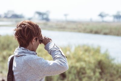Woman looking through binoculars while standing on field