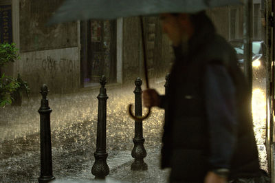 Man with umbrella walking on street during rainy season