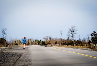Rear view of man walking on road against clear sky