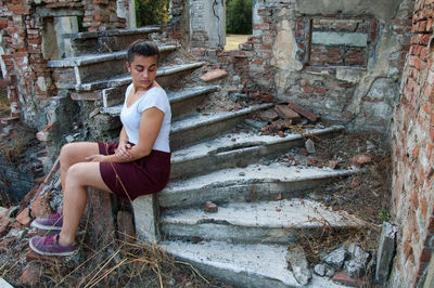 Woman sitting on steps of abandoned building