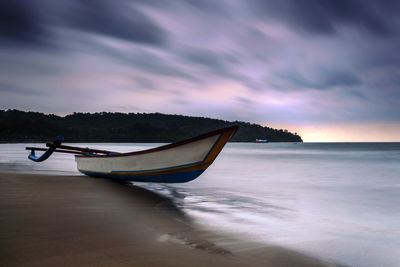 Boat moored on beach against sky during sunset