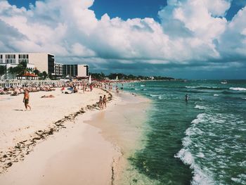 People on beach against cloudy sky