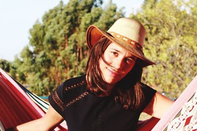 Portrait of young woman wearing hat against trees