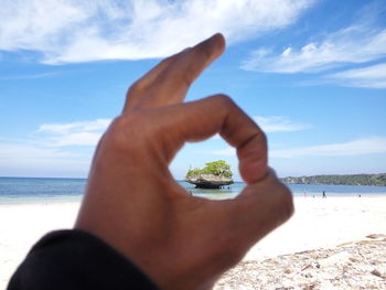 Island in sea against sky seen through ok sign