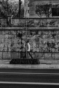 Rear view of man walking on sidewalk against wall