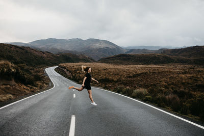 Woman jumping on road against sky