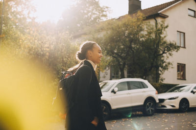 Side view of teenage girls walking against cars and house during autumn