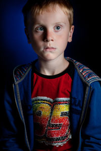 Portrait of boy standing against black background