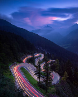 High angle view of light trails on road by mountains against sky