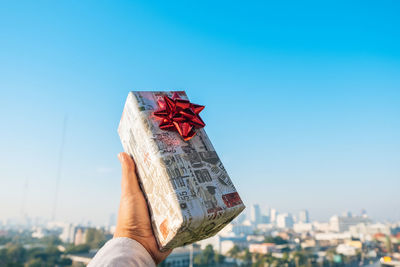 Close-up of human hand holding wrapped gift against sky