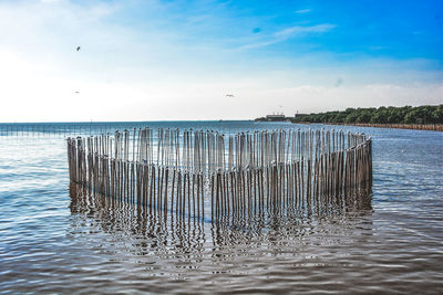 Wooden posts in sea against sky