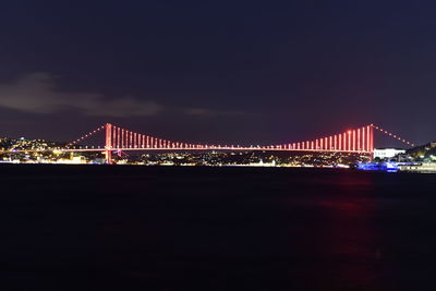 Illuminated bridge over river in city at night