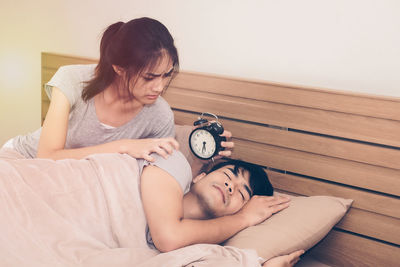 Woman holding alarm clock by sleeping man on bed