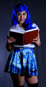 Young woman holding book against blue wall