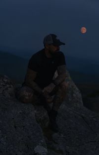 Man standing on rock by sea against sky at night