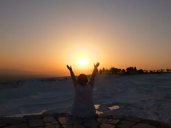 Rear view of woman standing on shore during sunset