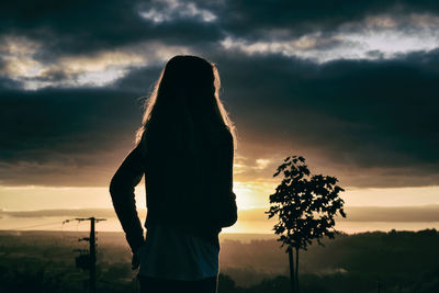 Rear view of woman standing against cloudy sky during sunset