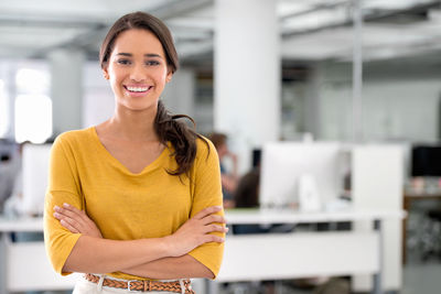 Happy woman with arms crossed standing in office