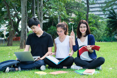 Friends studying while sitting on grassy field at park