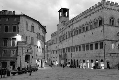 People on street amidst buildings in city against sky