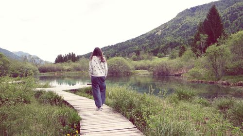 Rear view of woman standing by lake against clear sky